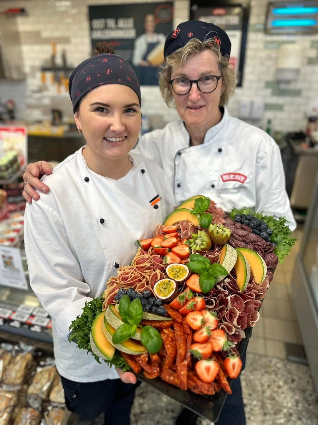 To ansatte i ferskvareavdelingen holder et spekefat med melon, jordbær, chorizo og spekeskinke.