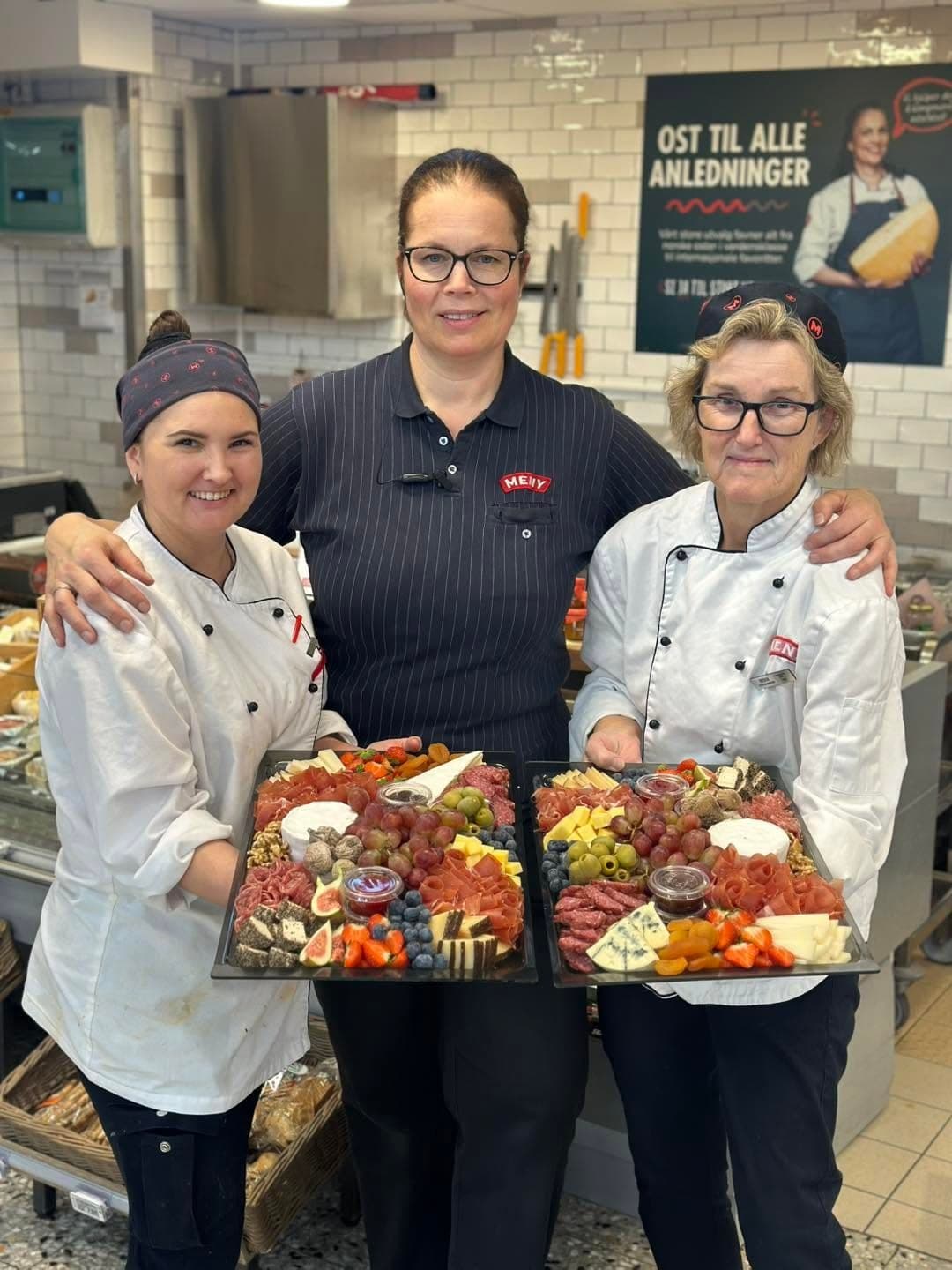 Tre ansatte i MENY Blinken holder to ostefat med brie, oliven, druer, fiken og spekemat.