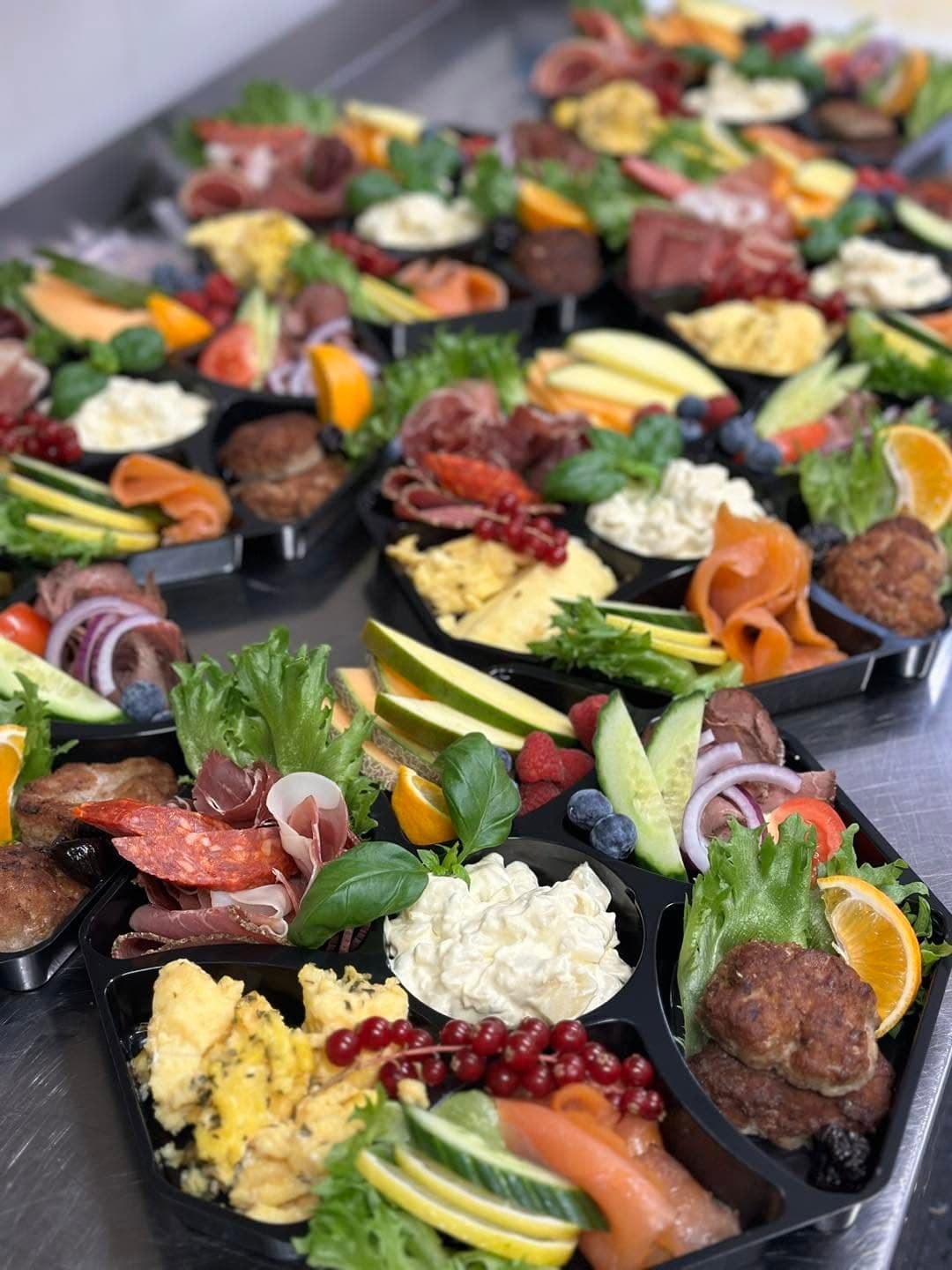 Koldtbord porsjonert i esker med spekemat, eggerøre, potetsalat, kjøttkaker, røkelaks, melon og bær.