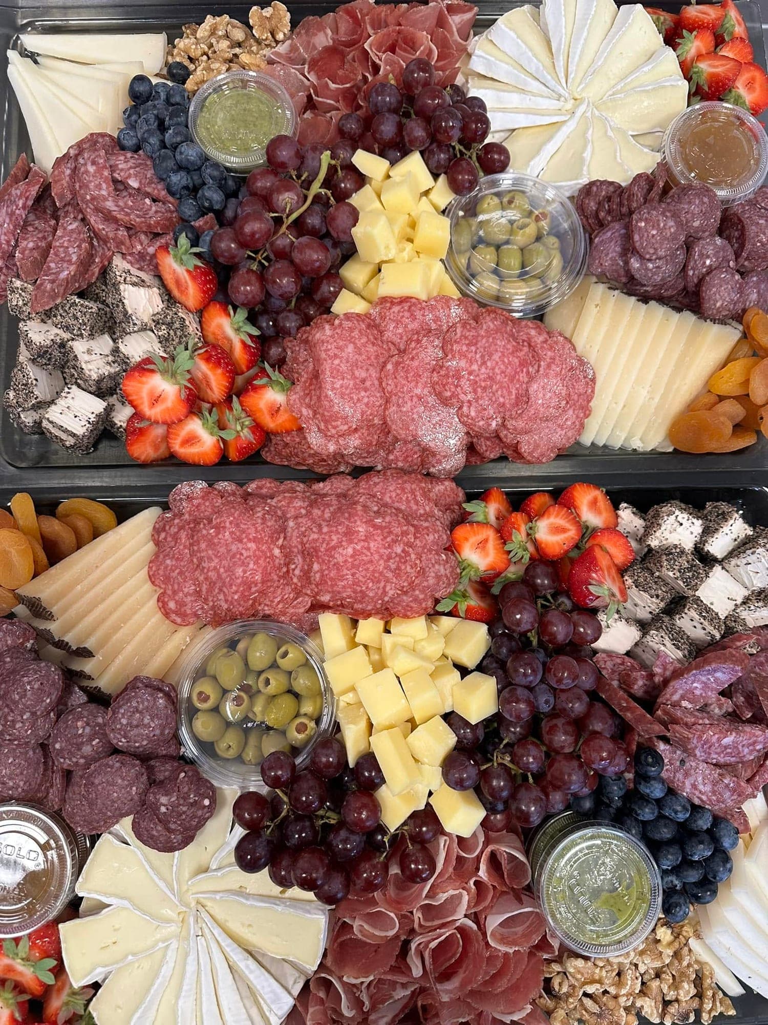 To ostefat sett ovenfra med brie, fast ost i terninger, salami, druer, jordbær, oliven, valnøtter og syltetøy.